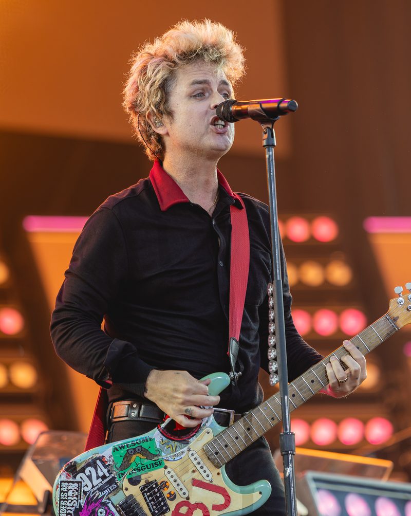 Billie Joe Armstrong singing and playing Blue, his sticker-covered Stratocaster-style guitar, at the Isle of Wight Festival, 23 June 2024.