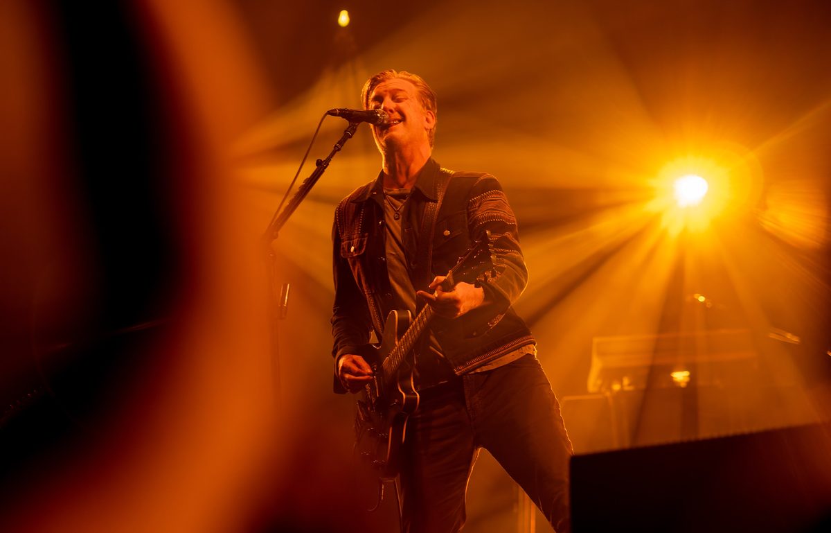 Josh Homme singing and playing guitar in amber stage light, Resorts World Arena, Birmingham, 19 November 2023.