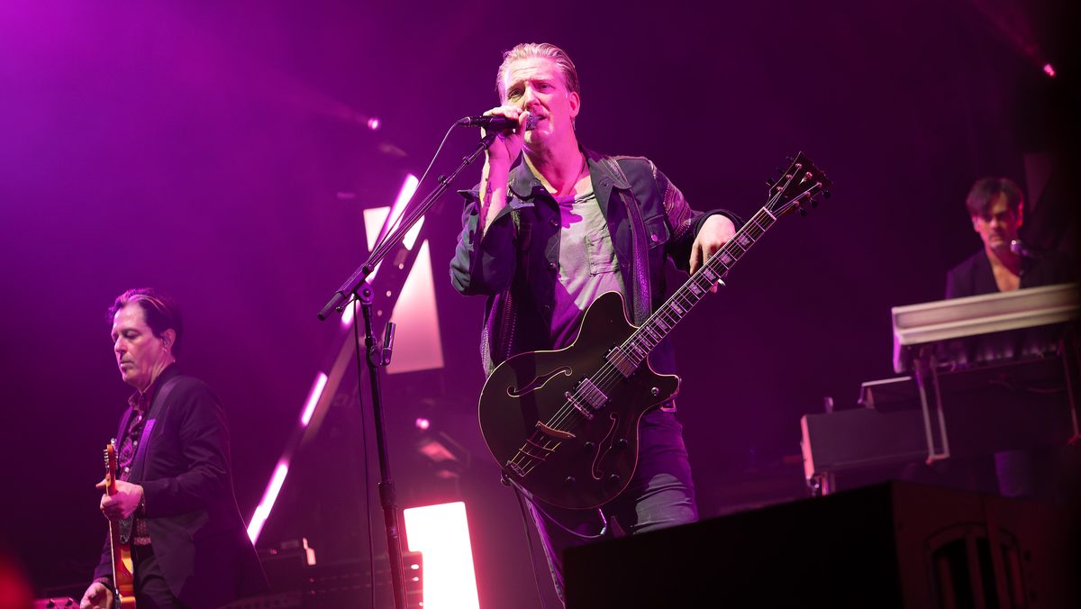 Josh Homme singing with a hollow-body guitar, Troy Van Leeuwen on guitar and Dean Fertita at the keyboards, Resorts World Arena, Birmingham, 19 November 2023.