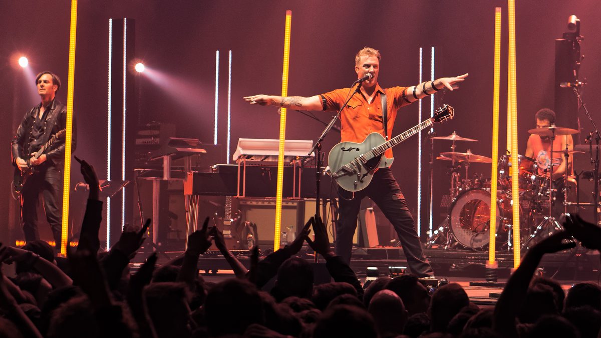 Josh Homme with arms spread and his guitar on, Troy Van Leeuwen on the left and Jon Theodore on drums, SSE Arena Wembley, London, 18 November 2017.