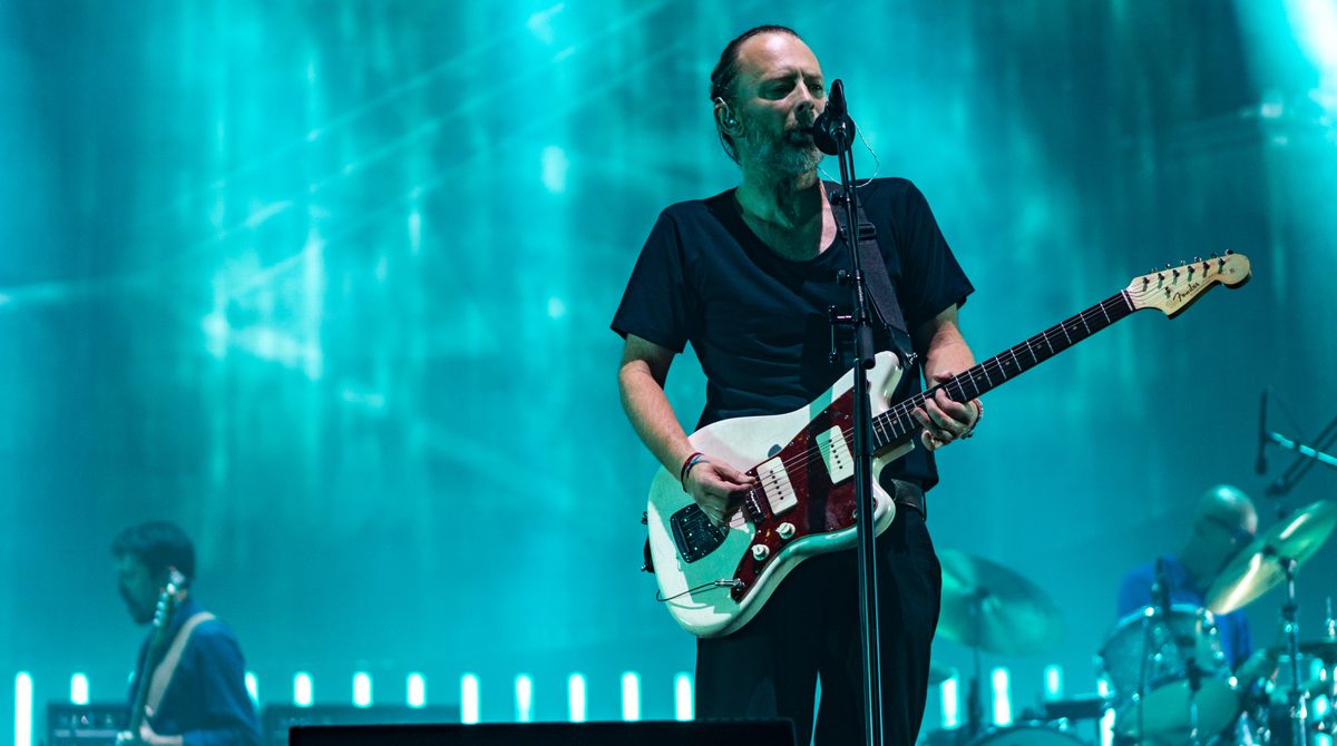 Thom Yorke singing and playing his white Fender Jazzmaster with Radiohead at the Bell Centre in Montreal on 17 July 2018, a guitarist and a drummer behind him.